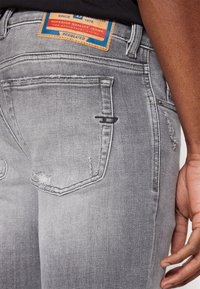 Jeans de denim gris con un aspecto desgastado, que cuentan con una etiqueta de cuero en la cintura, detalles de costura y dos bolsillos traseros.