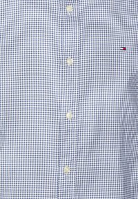 Camisa azul y blanca a cuadros hecha de tela, con cuello clásico, seis botones blancos y un pequeño logo en el pecho.