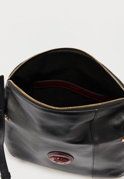 Sort læderhåndtaske med guldlynlås, delvist åben, der viser mørk indre og præget cirkulært logo foran.