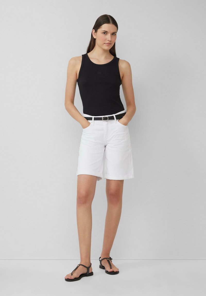 Schwarzes geripptes Tanktop, weiße knielange Shorts mit Umschlägen, schwarzer Gürtel mit Metallschnalle und schwarze flache Sandalen, vor einem grauen Hintergrund präsentiert.