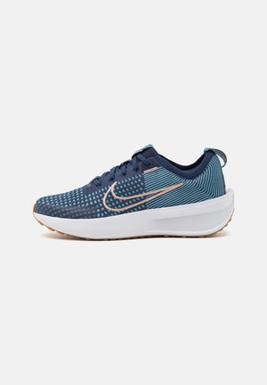Chaussure de course tricotée bleu marine et bleu sarcelle avec une semelle épaisse blanche et un logo swoosh couleur pêche sur le côté, présentée sur fond blanc.