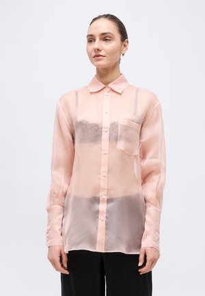 Γυναίκα που φορά διαφανές ροζ ανοιχτόχρωμο πουκάμισο με μακριά μανίκια και κουμπιά, με τσέπη στο στήθος, και μαύρα εσώρουχα ορατά από μέσα.