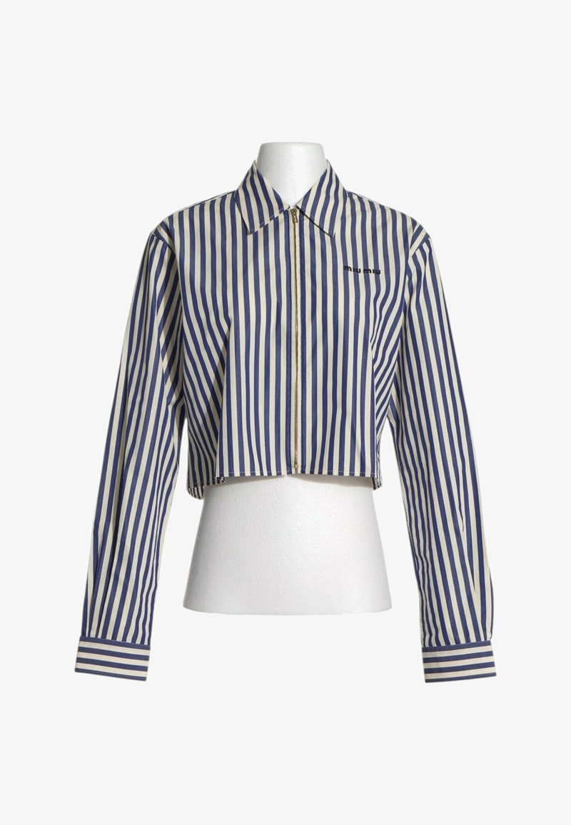 Veste courte à manches longues avec des rayures verticales bleues et blanches et une fermeture éclair frontale sur un torse de mannequin blanc.