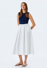Débardeur bleu marine associé à une jupe plissée blanche longueur genoux. La tenue présente un corsage ajusté et un tissu fluide. Sandales dorées.