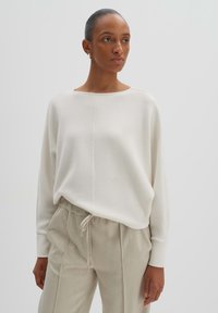 Maglione in morbido tessuto avorio con vestibilità rilassata, scollo a barca e maniche lunghe. Abbinato a pantaloni beige leggeri con coulisse.