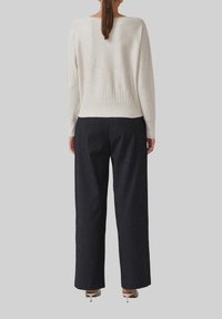 Lichtbeige gebreide trui met een geribbelde tailleband, gecombineerd met donker gestreepte wijde broek. Eenvoudig, gestructureerd stoffenontwerp.