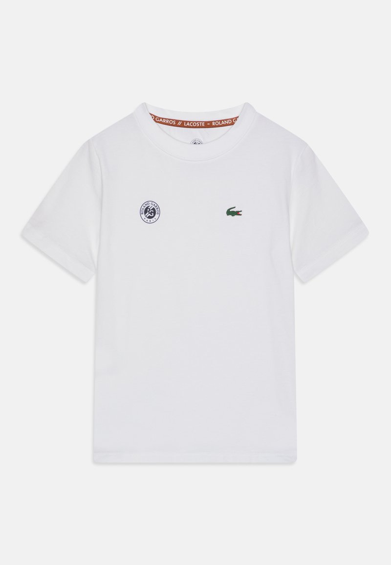 T-shirt en coton blanc à manches courtes, avec un col rond, un logo crocodile vert et un petit emblème circulaire bleu sur la poitrine.