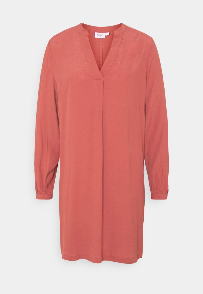 Robe tunique corail à manches longues avec encolure en V, coupe ample et poignets froncés sur fond uni clair.