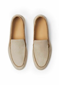 Scarpe slip-on in suede beige con una superficie liscia, punta arrotondata e dettagli in suede marrone a contrasto lungo i bordi e la fodera.