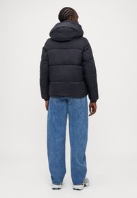 Svart boblejakke med hette, med en kviltet tekstur og en litt løs passform. Kombinert med vide blå denimjeans.