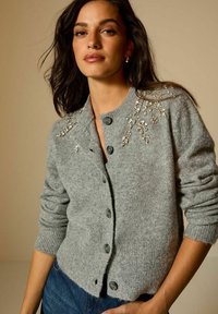 Cardigan grigio in lana con scollo rotondo, decorato con perline e motivi floreali sulle spalle, dotato di sei bottoni frontali e polsini a coste.