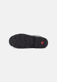 Black rubber shoe sole with a textured zigzag pattern and a red circular accent. Durable and designed for grip and traction.