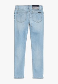 Ljust blå denimjeans med slim fit, med bakfickor, midjebandsmärke och subtila sömdetaljer. Slät textur, rak bendesign.