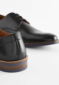 Chaussures habillées noires en cuir avec une finition lisse, dotées d'un petit talon, de coutures élaborées et d'un accent texturé au talon.