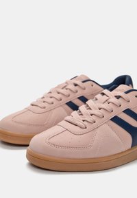 Helle rosa Sneakers mit marineblauen Akzenten. Glattes, lederähnliches Material, Schnürdesign und eine Gummisohle. Robuste Bauweise mit Perforationen.