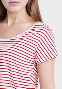 Camiseta de manga corta a rayas con un amplio escote en forma de barco, que presenta rayas horizontales alternas rojas y blancas sobre una tela suave.