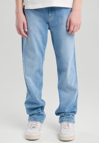 Hellblaue Jeans aus Denim mit relaxed Fit und geraden Beinen. Getragen mit weißen Sneakers mit durchlöchertem Design.