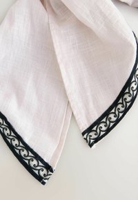 Tissu en lin rose clair avec une bordure brodée noire et blanche présentant un motif tourbillonnant décoratif le long des bords.