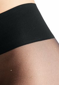 La fascia nera opaca si trasforma in una calza trasparente e testurizzata con un motivo a griglia fine, caratterizzata da piccole lentiggini dorate sulla superficie.