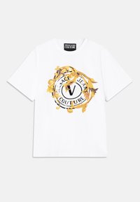 Hvit bomull T-skjorte med et sentralt grafisk motiv i svart og gull, med et sirkulært design og teksten "Versace Jeans Couture". Korte ermer.