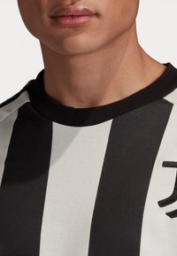 Sort- og hvidstribet sweater med rund hals og ribbet krave. Har et struktureret stof og en diskret logo detalje på forsiden.