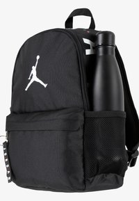 Črn nahrbtnik iz trpežnega blaga, ki vsebuje velik glavni predal, mrežast stranski žep in bel Jordanov logotip. Vključuje stekleničko za vodo.