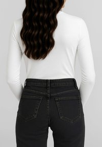 Top bianco a maniche lunghe con scollo rotondo, abbinato a jeans neri a vita alta con due tasche posteriori e cuciture tono su tono.