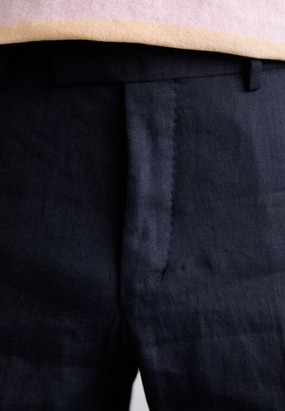 As calças de linho azuis apresentam um corte plano, bolsos laterais e costura limpa, combinadas com uma parte superior em rosa claro e bege visível acima.