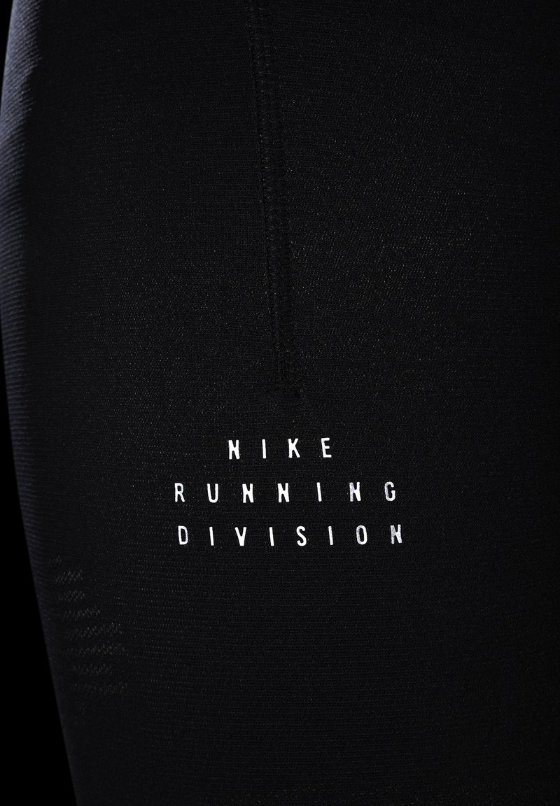 Leggings de sport noires en tissu lisse, de forme ajustée, avec un logo imprimé blanc indiquant "NIKE RUNNING DIVISION."