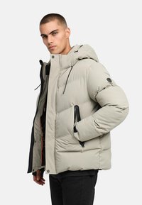 Ljusgrå pufferjacka med huva, med zippered fram, sidofickor och svarta detaljer. Slät textur och quiltat mönster.