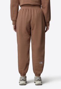 Bruna sweatpants med elastisk midja och avslut, med en liten vit logotyp på nedre benet. Tillverkade av mjukt tyg, avslappnad passform.