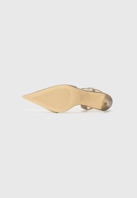 Beige high-heeled shoe with a pointed toe, textured sole, and slender straps. Features a smooth finish and a square accent on the heel.