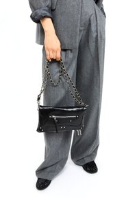 Črna usnjena torbica z srebrnim okovjem, ki ima sprednji žep z zadrgo in kroglice, nosi se na verižnem ročaju, kombinirana s sivo prugastimi širokimi hlačami.
