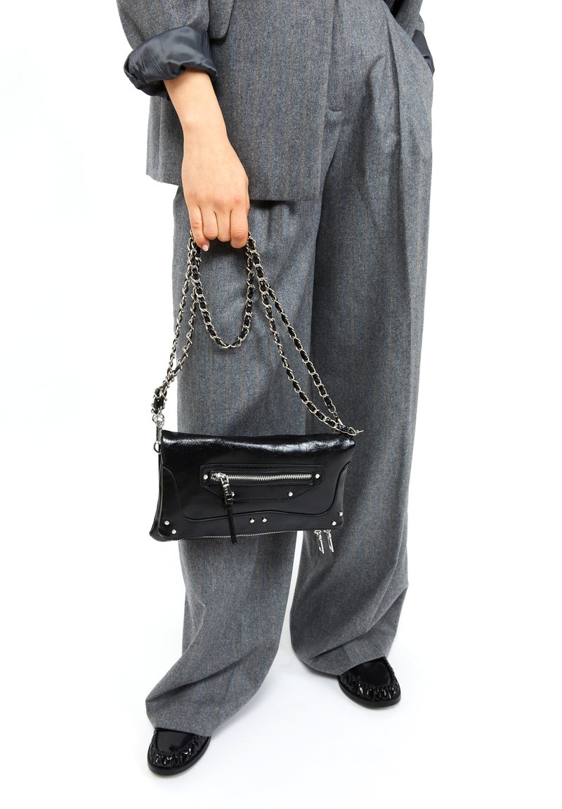 Črna usnjena torbica z srebrnim okovjem, ki ima sprednji žep z zadrgo in kroglice, nosi se na verižnem ročaju, kombinirana s sivo prugastimi širokimi hlačami.