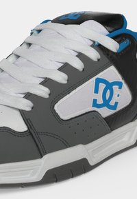Gros plan d'une basket DC grise, noire, blanche et bleue avec des lacets blancs et le logo DC sur le côté.