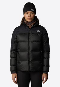 Zwarte pufferjack met een ritssluiting aan de voorkant, gemaakt van glanzende stof. Heeft een effen bovenste deel, elastische manchetten en het logo van The North Face.