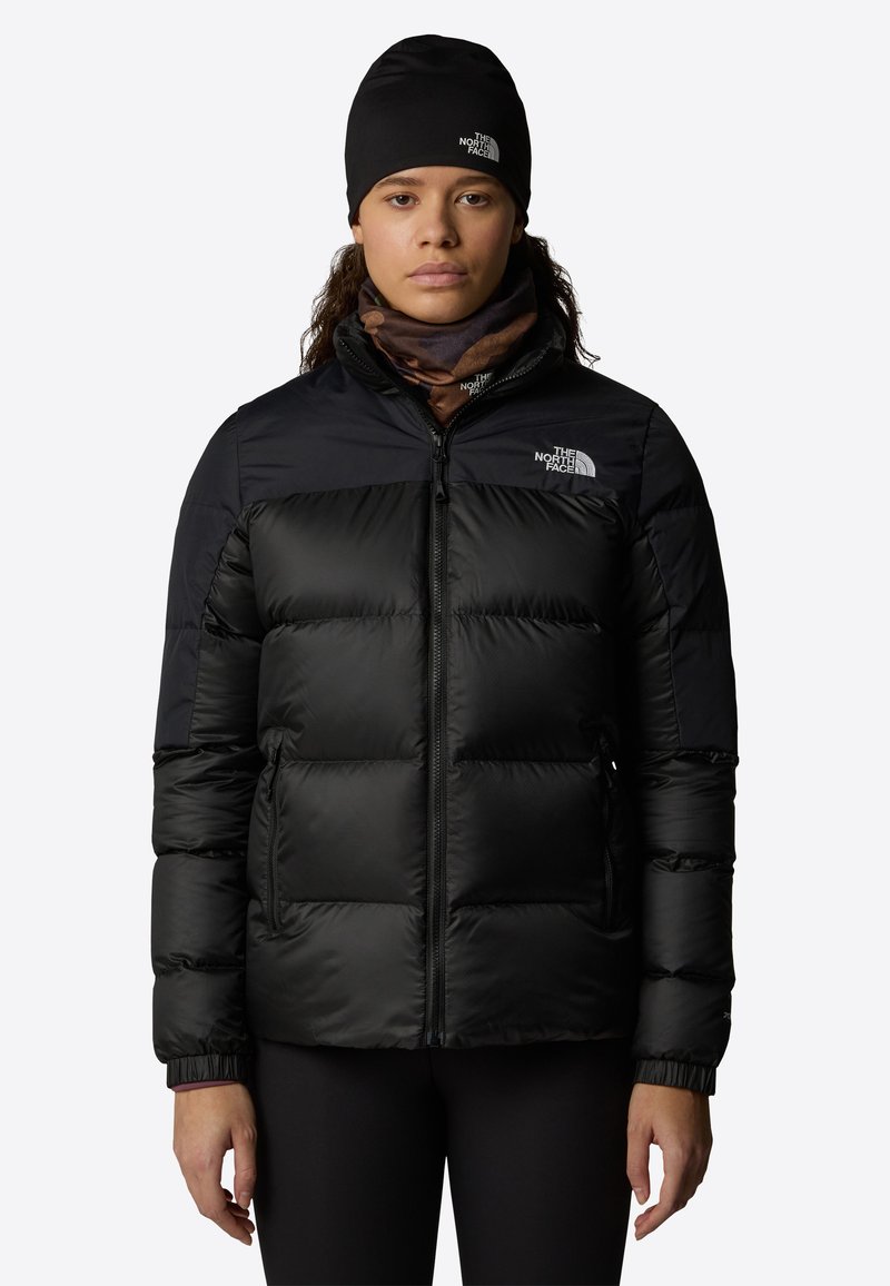 Zwarte pufferjack met een ritssluiting aan de voorkant, gemaakt van glanzende stof. Heeft een effen bovenste deel, elastische manchetten en het logo van The North Face.