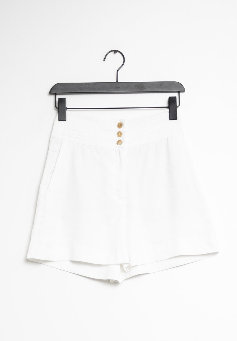 Shorts blancs en tissu lisse, avec une ceinture élastique, trois boutons dorés à l'avant et des poches latérales.