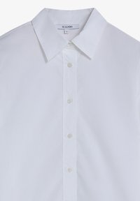 Camisa de cuello blanco hecha de tela suave; cuenta con un cierre de botones en la parte delantera con cinco botones y una etiqueta de la marca cosida en el interior del cuello.