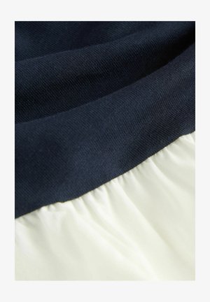 Navy blue ribbed knit fabric at the top transitions to soft, gathered cream fabric below, showcasing smooth textures and contrasting colors.