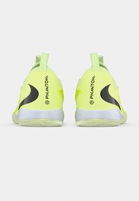 Jasnożółte buty sportowe z czarnymi akcentami, gładką górną częścią, amortyzującą podeszwą oraz pętelkami na pięcie ułatwiającymi zakładanie.