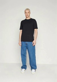 T-shirt nera a maniche corte in cotone, abbinata a jeans blu a taglio comodo e sneaker bianche con accenti neri.
