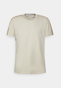 Ljust beige kortärmad t-shirt med rund halsringning, med kontrasterande bruna detaljer längs axlarna och varumärkestryck. Mjuk tygtextur.