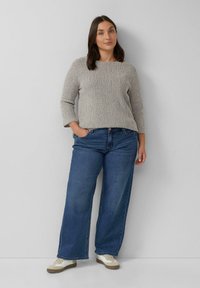 Grijze gebreide trui met een ronde halslijn en driekwart mouwen, gecombineerd met lichtblauwe wijde jeans en witte sneakers.