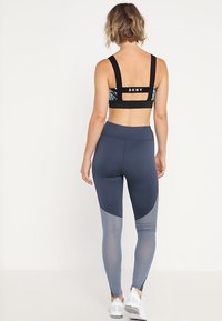 Top sportivo DKNY in nero con schiena a fantasia, abbinato a leggings blu navy con pannelli trasparenti e design a blocchi di colore curvi.
