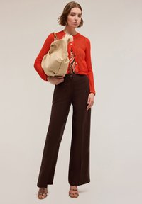Cardigan rossa lavorata a maglia con bottoni, pantaloni marroni a vita alta, borsa beige inclinata e top fantasia, indossato con tacchi a strappo.