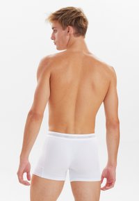 Boxer a vita bassa bianchi realizzati in tessuto morbido, caratterizzati da una vestibilità aderente, una texture liscia e una cintura elastica con logo. Modello mostrato di spalle.