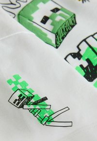 Figure de squelette pixelisé stylisé en vert et noir allongé sur un tissu blanc avec des éléments de design en blocs.