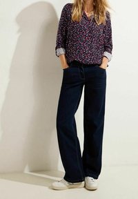 Blouse bleu marine à motifs avec un col en V et des manches trois-quarts, associée à un jean large bleu foncé et des baskets blanches. Tissu texturé.