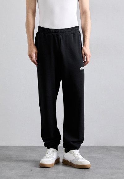 Sorte sweatpants med elastisk talje, sidelommer og hvid logo detalje. Båret med hvide og grå sneakers. Minimalistisk design.